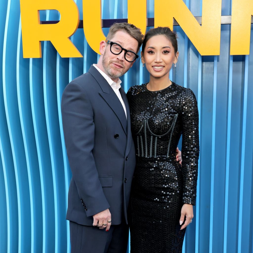 Macaulay Culkin und Brenda Song posieren im Anzug und schwarzem Pailletten-Abendkleid auf dem blauen Teppich der Premiere von Netflix' "Running Point"