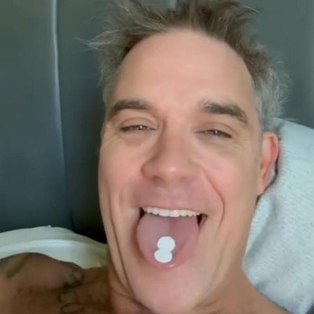 Robbie Williams zeigt zwei Minzpastillen, die er auf der Zunge hat