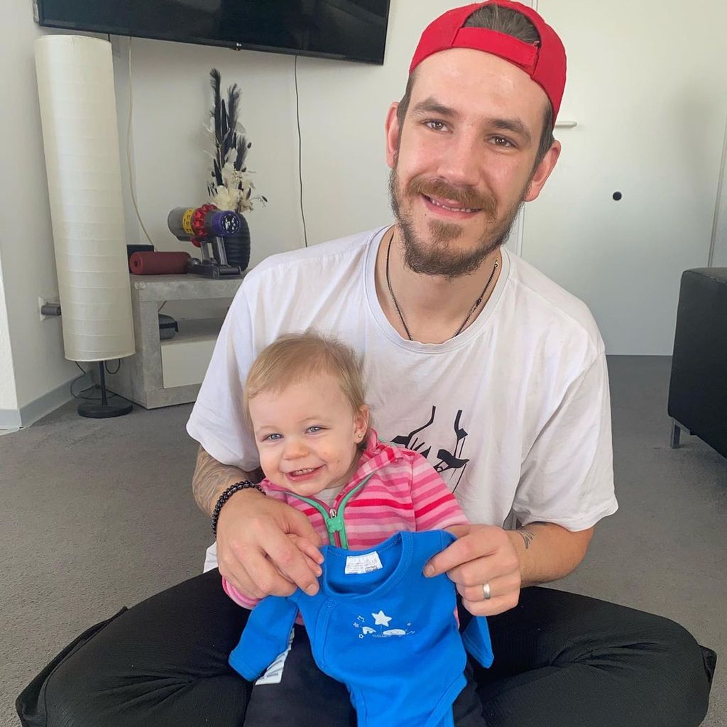 Tim Katzenbauer und Töchterchen Haylie Emilia zeigen einen blauen Strampler