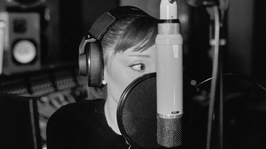 Ariana Grande hinter einem Mikrofon im Studio.