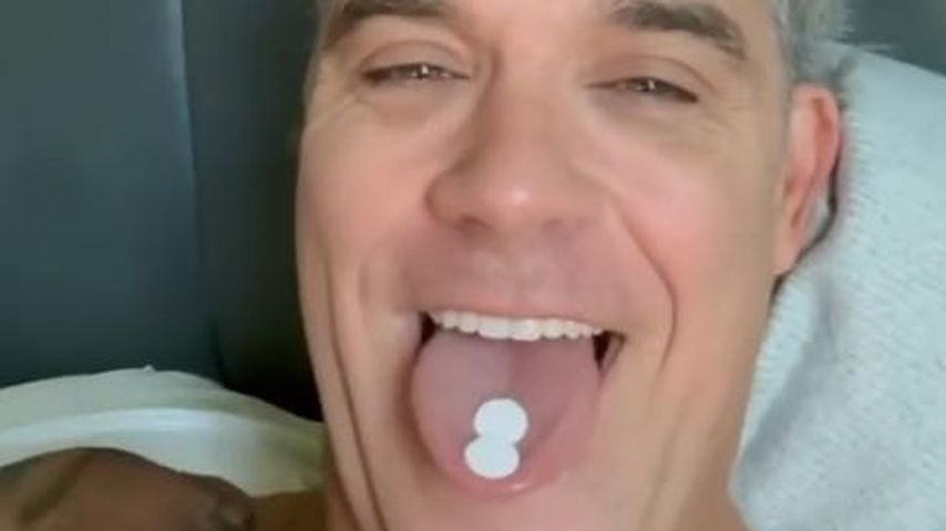 Robbie Williams zeigt zwei Minzpastillen, die er auf der Zunge hat